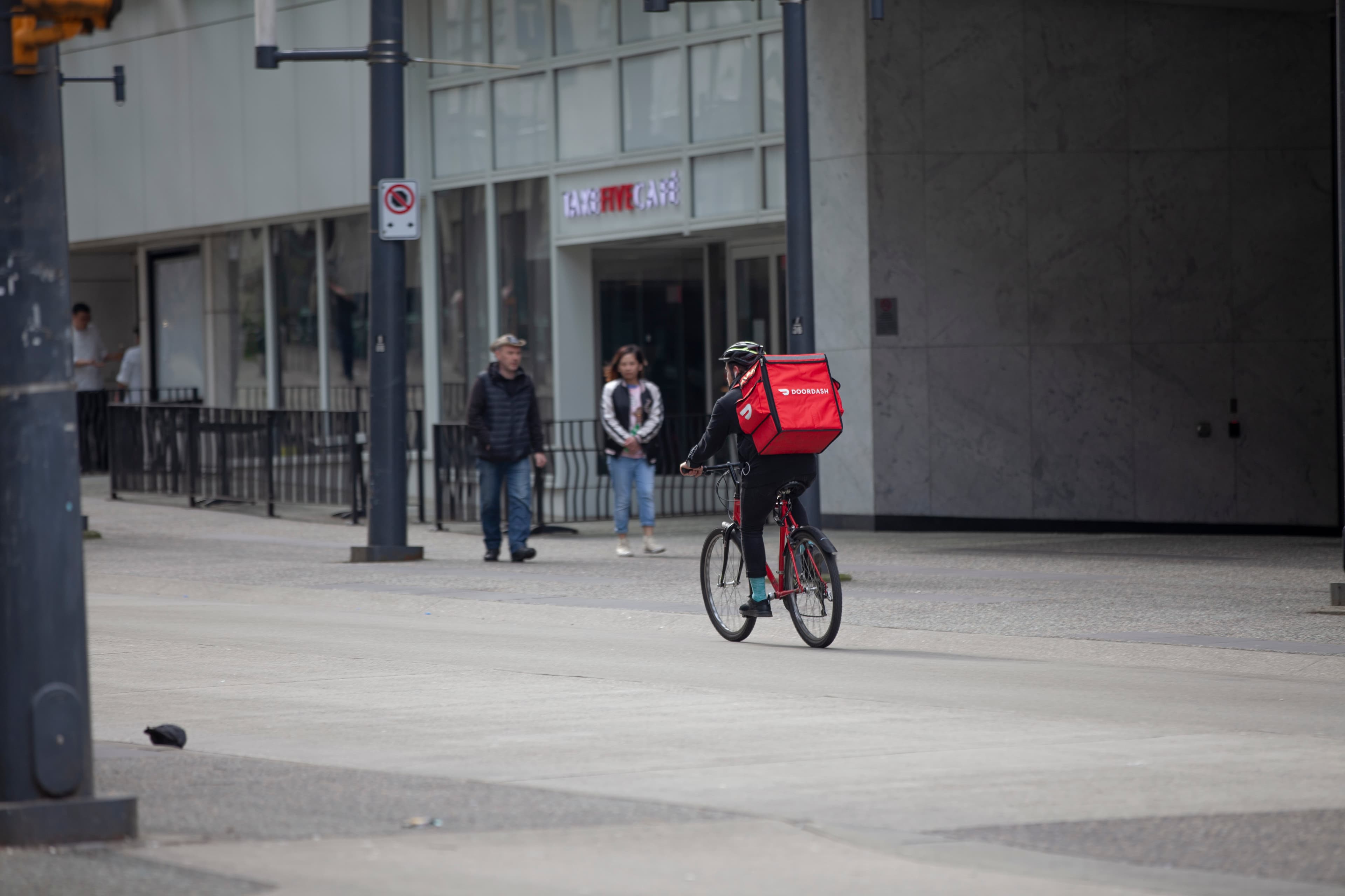 A bicycle courier carrying a red DoorDash delivery backpack on Granville Street in downtown Vancouver.