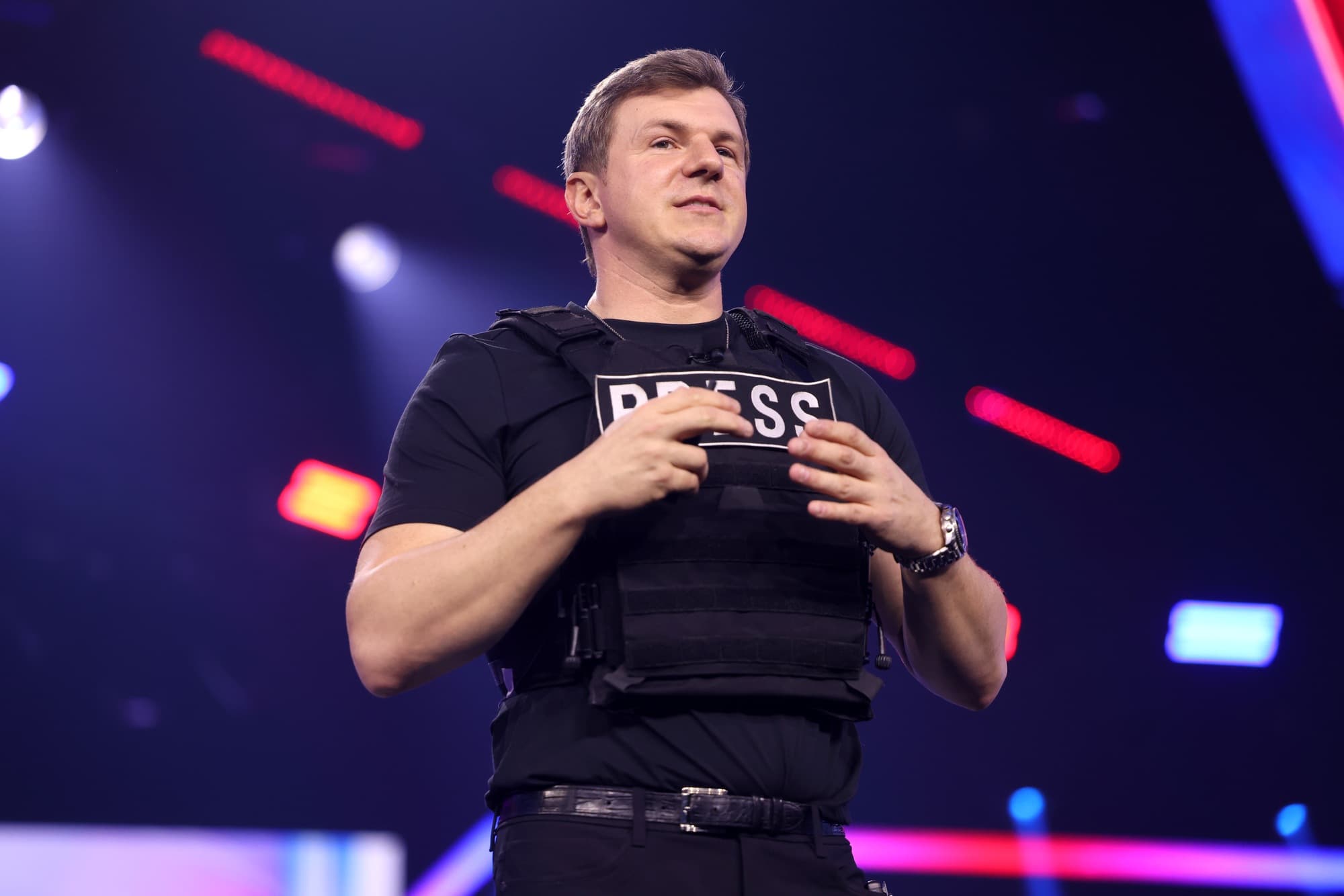 James O’Keefe speaks onstage while wearing a black vest marked Press at a December 2024 event.