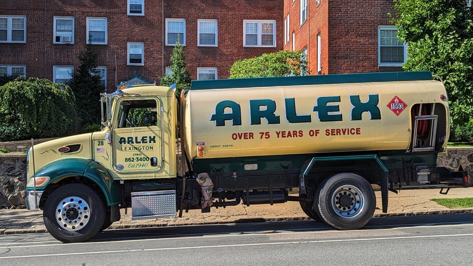 A cream and green heating oil delivery truck parked on a residential street in front of a brick apartment building in Arlington, Massachusetts, in 2023.