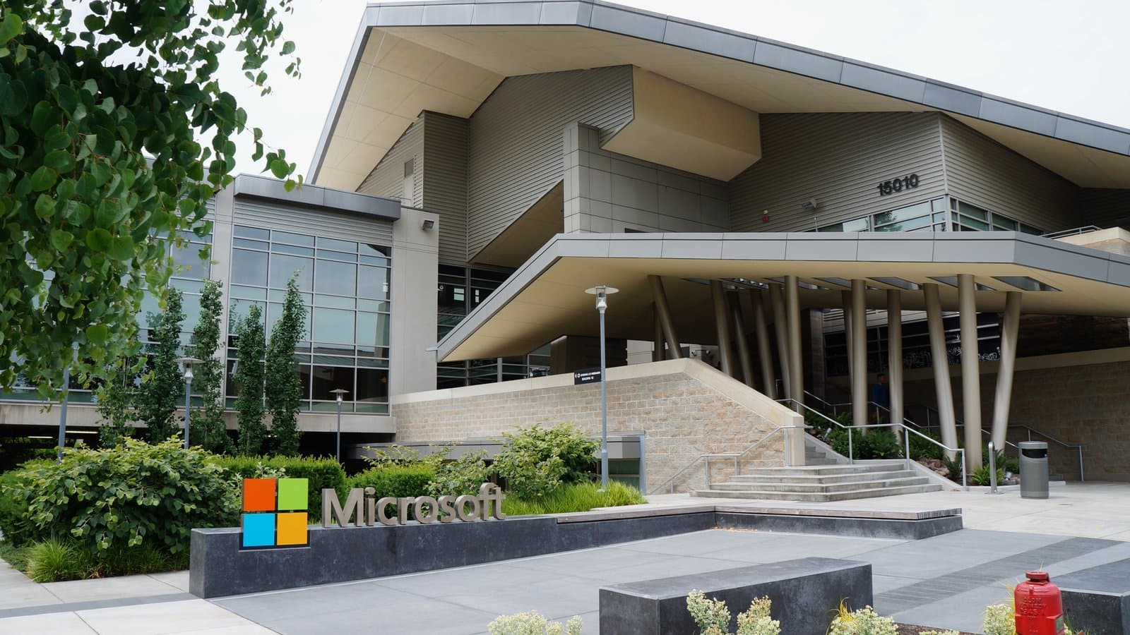 Microsoft's Building 92 in Redmond, Washington, a modern gray building with an angled roof and columns, with the Microsoft logo sign and shrubs in front.