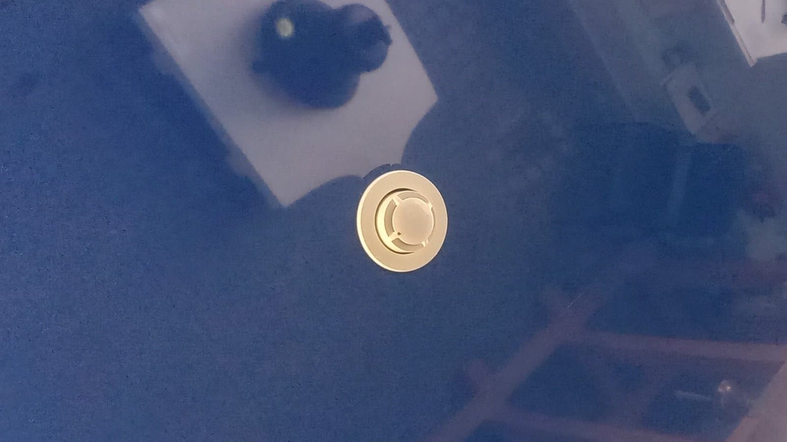 A round smoke detector mounted on a glossy blue ceiling, photographed in July 2023.